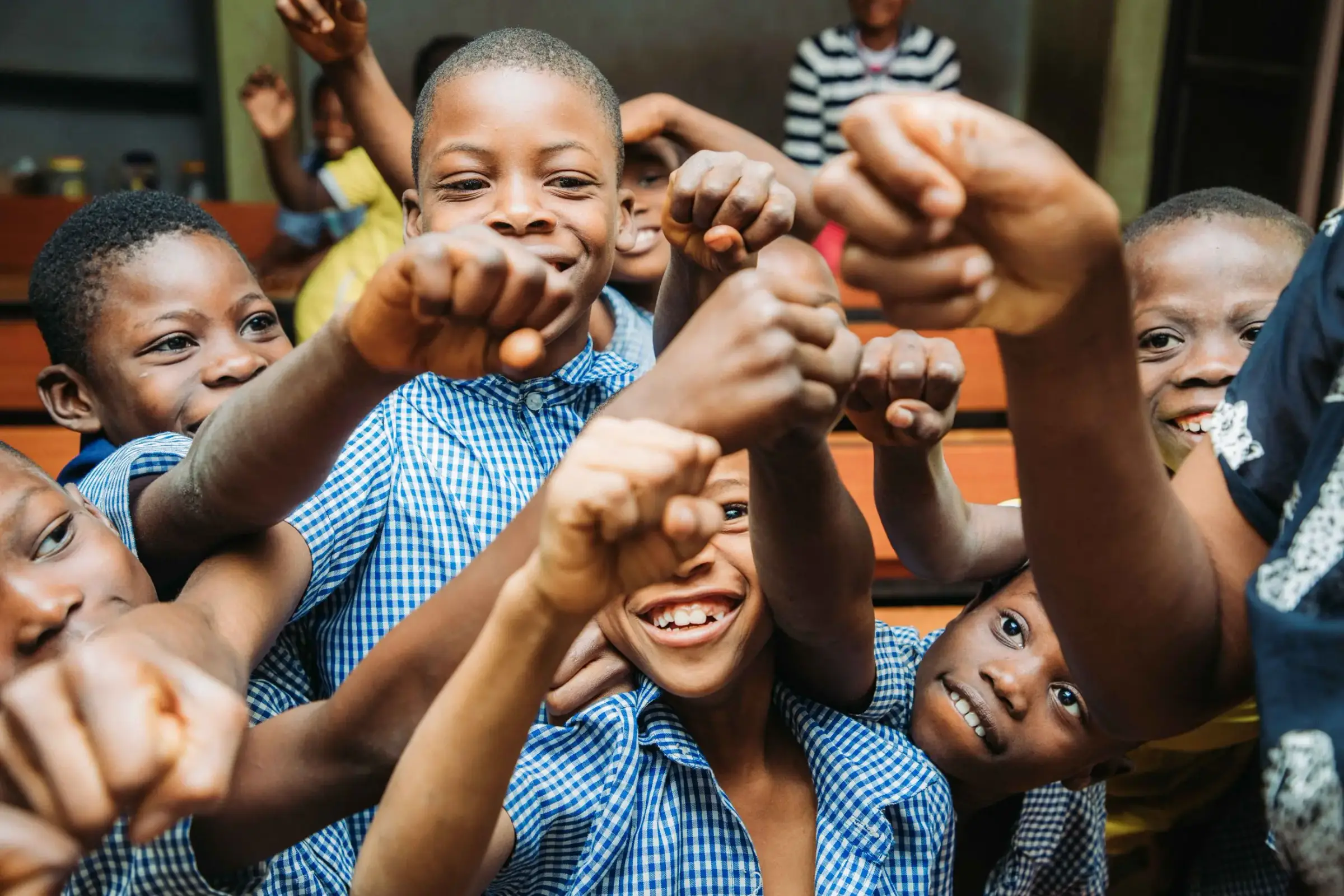 Schoolchildren in blue gingham uniforms grinning and raising their fists